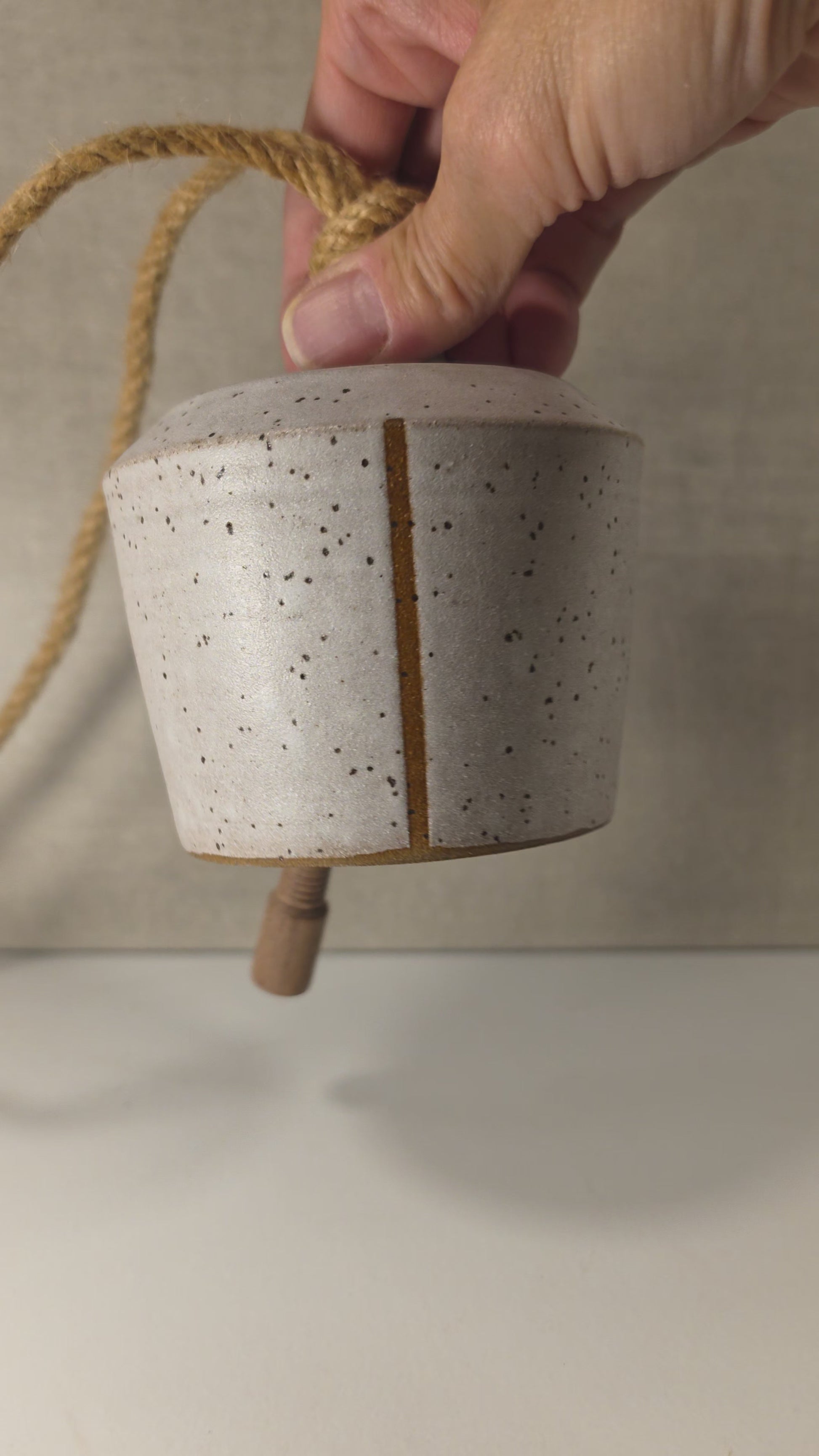 ringing of small handmade ceramic bell with stripe, glazed in a matte white speckled finish